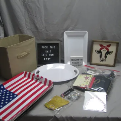 Sale Photo Thumbnail #292: Collection of home decor items including an American flag tray, white serving platters, novelty signs, a tan storage cube, and party supplies.
