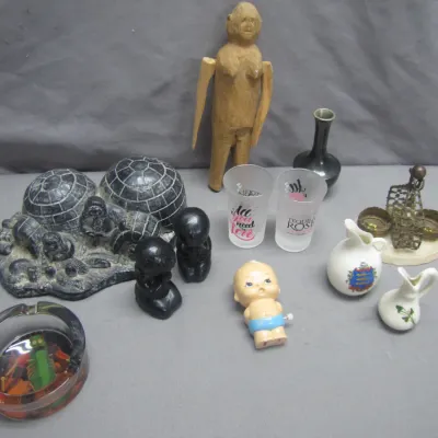 Sale Photo Thumbnail #85: Eclectic lot of vintage collectibles, including a carve wood figure, an igloo snow scene sculpture, small pottery pitchers, shot glasses, and a glass ashtray.