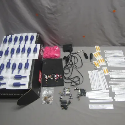 Sale Photo Thumbnail #24: Collection of tattoo supplies, including coil machines, power supply and cords, disposable grips, needles in sterile packaging, and rubber bands.