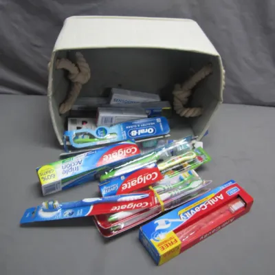 Sale Photo Thumbnail #173: Fabric storage bin filled with an assortment of new dental care products, including toothbrushes and tubes of toothpaste from brands like Colgate, Oral-B, and Sensodyne.