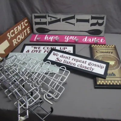 Sale Photo Thumbnail #280: Collection of decorative wall signs featuring humorous and inspirational quotes alongside a stack of metal display stands.