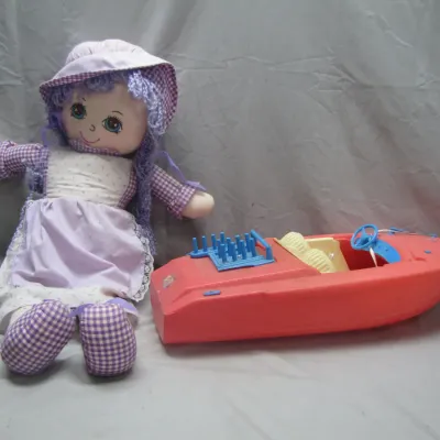 Sale Photo Thumbnail #224: Vintage soft rag doll with purple hair and gingham outfit paired with a red plastic toy speedboat, circa 1970s-1980s.