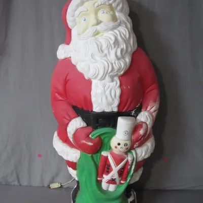 Sale Photo Thumbnail #125: Vintage illuminated Santa Claus blow mold figure holding a toy soldier and green bag, showing light paint wear.