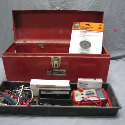 Sale Photo Thumbnail #195: Vintage red metal toolbox with a latch closure, containing a removable tray filled with electrical testing tools including a Craftsman digital multimeter, wiring, and a packaged PowerCare blade sharpener.