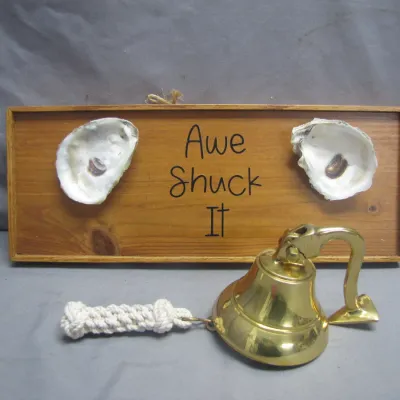 Sale Photo Thumbnail #97: Nautical-themed wooden wall plaque reading "Awe Shuck It" flanked by oyster shells, paired with a polished brass ships bell featuring a braided rope clapper pull.