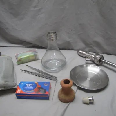 Sale Photo Thumbnail #229: Disassembled modern stainless steel and clear glass hookah set, including clay bowl, tray, tongs, and a box of charcoal.