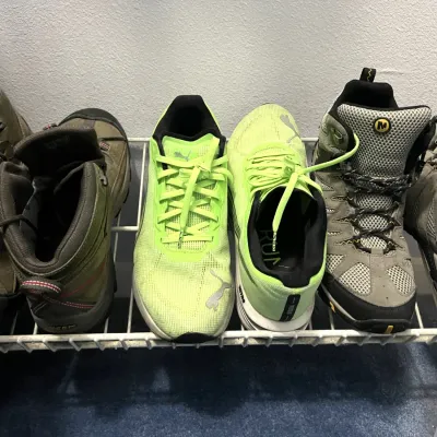 Sale Photo Thumbnail #37: Selection of men's athletic footwear on a shoe rack, including Keen hiking boots, bright yellow Puma running shoes, and Merrell hiking boots.