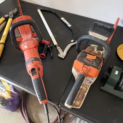 Sale Photo Thumbnail #20: Selection of outdoor power tools and hand tools, including an orange electric hedge trimmer, a Stihl chainsaw, loppers, and a bow saw.