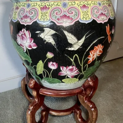 Sale Photo Thumbnail #65: Large Chinese porcelain fishbowl planter featuring hand-painted lotus flowers and birds against a black ground, displayed on a carved wooden base.