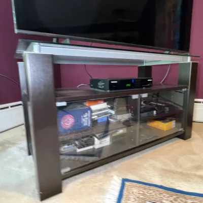 Sale Photo Thumbnail #33: Modern dark espresso wooden media console featuring glass shelving, sliding glass doors, and a top glass surface supporting a flat-screen television.