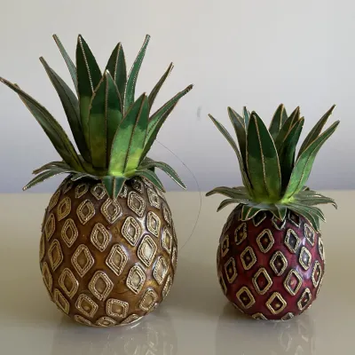 Sale Photo Thumbnail #63: Pair of vintage enamel and metal pineapple-shaped trinket boxes or decorative figurines, featuring intricate gold filigree detailing on the body and leafy tops.
