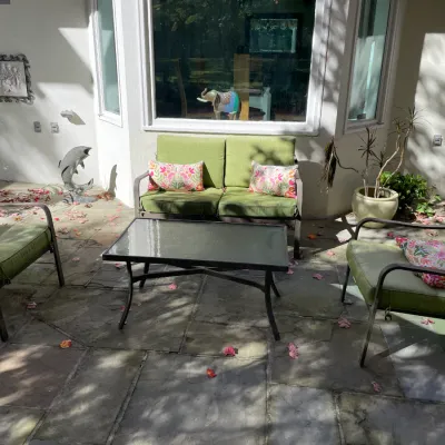 Sale Photo Thumbnail #24: Four-piece metal patio furniture set including a loveseat, two armchairs with green cushions and floral accent pillows, and a glass-top coffee table.