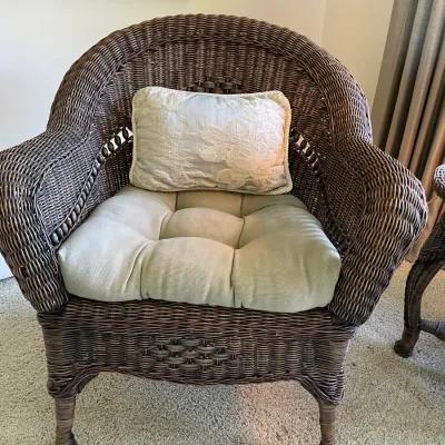 Sale Photo Thumbnail #59: Dark brown woven wicker armchair with a rounded back, featuring a tufted seat cushion and an embroidered decorative throw pillow.