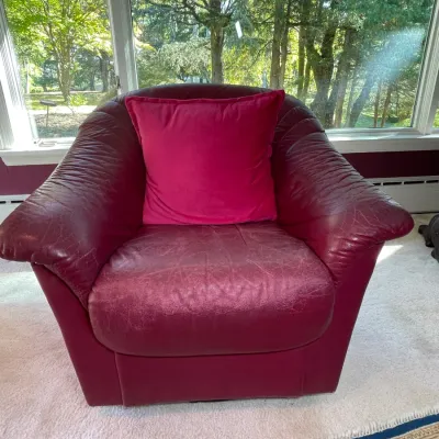 Sale Photo Thumbnail #29: Vintage deep red leather armchair with flared rolled arms, gathered leather detailing, and a matching pink accent pillow, showing moderate wear and creasing on the seating surfaces.