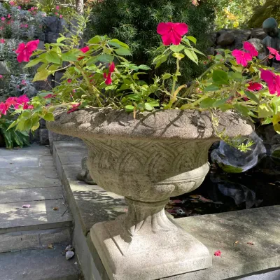 Sale Photo Thumbnail #13: Cast stone garden urn planter with weathered finish and woven relief pattern, filled with impatiens and evergreen foliage.