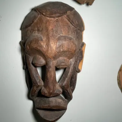 Sale Photo Thumbnail #70: Hand-carved African style wooden mask featuring prominent facial structures and open eye cutouts.