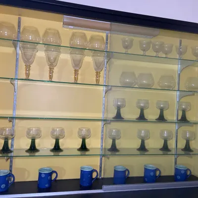Sale Photo Thumbnail #6: A wall-mounted glass display cabinet featuring vintage glassware, including green-stemmed Roemer wine glasses, oversized clear goblets, and blue ceramic mugs.