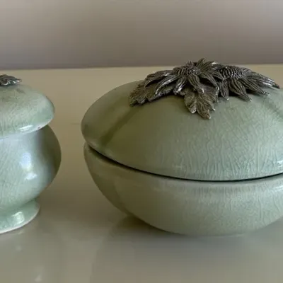 Sale Photo Thumbnail #62: Two green crackle-glaze ceramic trinket boxes featuring pewter floral and acorn lid accents, alongside a small white ceramic elephant figurine.