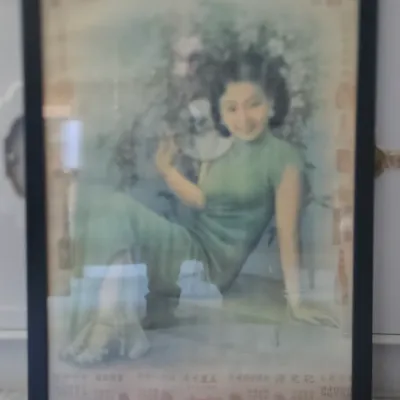 Sale Photo Thumbnail #41: Framed vintage Chinese advertising poster depicting a woman in a green cheongsam dress, set behind glass in a simple black frame.