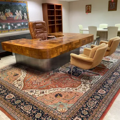 Sale Photo Thumbnail #79: Large executive office space featuring a butcher block U-shaped desk, a brown leather swivel chair, pair of tan upholstered guest chairs, and a large ornate Persian area rug.