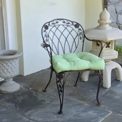 Sale Photo Thumbnail #46: Wrought iron patio armchair with rose motifs and green seat cushion, shown alongside a stone planter and concrete pagoda statue.