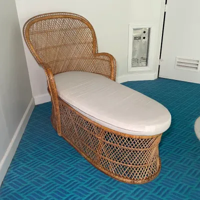 Sale Photo Thumbnail #77: Vintage wicker chaise lounge featuring an open lattice weave pattern, high curved back, and a light-colored fitted seat cushion.
