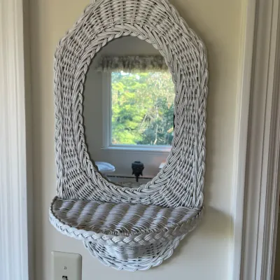 Sale Photo Thumbnail #58: Vintage white woven wicker wall mirror featuring an integrated shelf, mounted above a light switch.