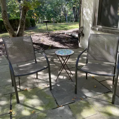 Sale Photo Thumbnail #16: Pair of contemporary outdoor mesh patio armchairs framed around a small mosaic-topped plant stand.