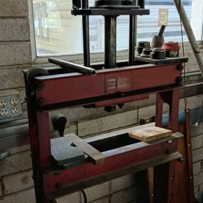 Red heavy-duty hydraulic shop press, showing typical wear from garage use.