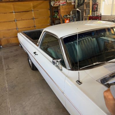 Vintage white classic pickup truck, likely a Ford Ranchero or Chevrolet El Camino, featuring a blue bench seat interior and chrome side...