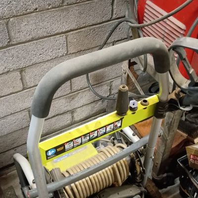 Ryobi pressure washer on a wheeled cart frame, showing normal wear and surface dust.