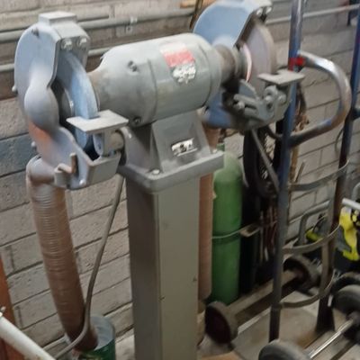 Vintage heavy-duty industrial bench grinder mounted on a matching pedestal stand, showing age-appropriate surface wear.