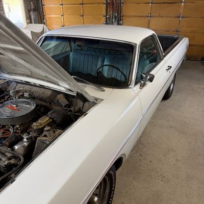 Classic white Ford Ranchero pickup with an open hood displaying the engine bay and a blue vinyl bench seat interior.