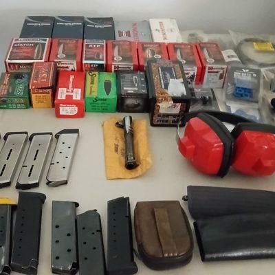 Collection of shooting supplies including handgun magazines, reloader bullets, red earmuffs, and related accessories.