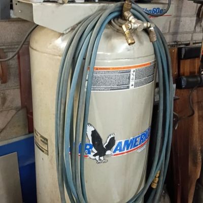 Air America stationary vertical air compressor featuring a 60-gallon tank, top-mounted motor, and wrapped blue hose.