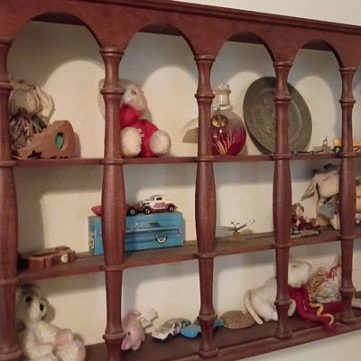 Vintage dark-stained wooden wall-hanging knick-knack shelf featuring turned spindle supports and arched openings, filled with small...