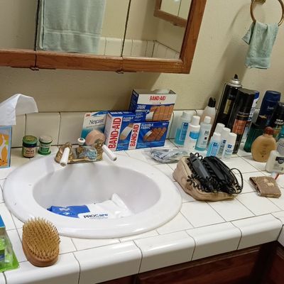 Assorted bathroom toiletries, personal care products, and grooming styling tools on a tiled vanity.