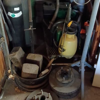 Collection of garage items including automotive brake rotors, gas cylinders, garden sprayers, and wooden blocks.