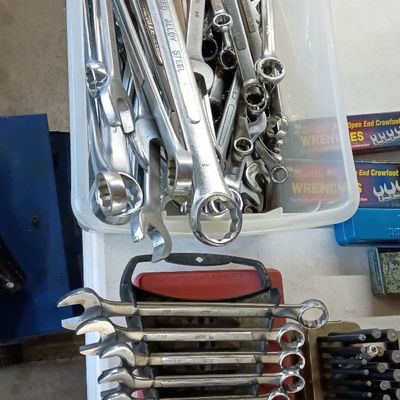 Assorted combination wrenches in a clear plastic bin alongside an organized rack of chrome wrenches and punch set.