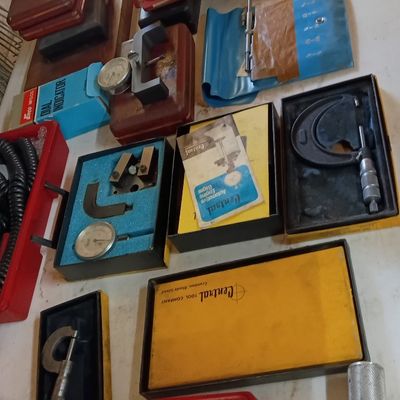Collection of vintage precision measuring tools, including micrometers, dial indicators, and calipers in fitted wooden and plastic cases.