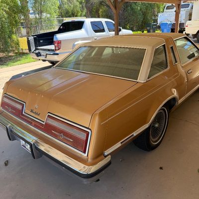 Vintage late 1970s Ford Thunderbird coupe in gold with a white vinyl landau roof, parked under a carport.