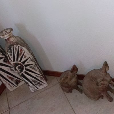Pair of tall distressed sunburst decorative floor vases alongside three rustic terracotta pig figurines arranged on a tile floor.
