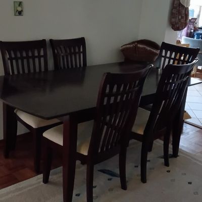 Dark wood dining table set with slatted-back chairs and light-colored upholstered seats, set over a patterned area rug.