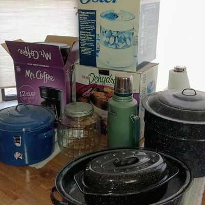 Collection of kitchen items including enamelware pots, a green Stanley thermos, glass jar, and boxed appliances like an Oster food...