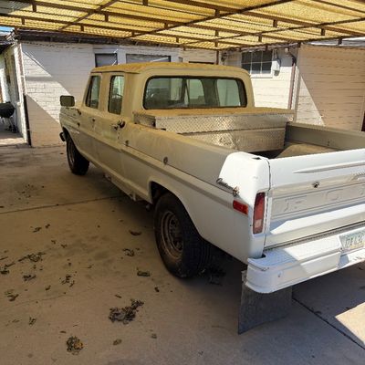 Vintage white Ford F-series crew cab pickup truck parked under a carport, featuring a diamond-plate bed toolbox.