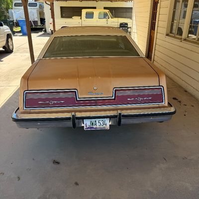 Rear view of a 1977-1979 Ford Thunderbird coupe in gold with a vinyl roof, parked under a carport.