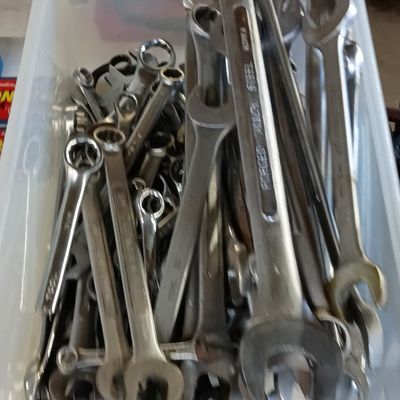 Clear plastic storage bin filled with an assortment of chrome combination wrenches in various sizes.