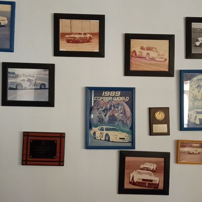 Collection of framed vintage race car memorabilia, including photos of race car #75, awards, plaques, and a 1989 Copper World Classic...