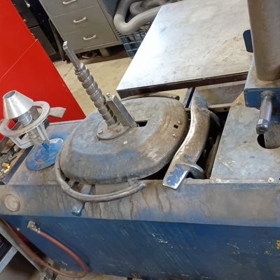 Vintage blue mechanical tire changer machine with center post and bead breaker attachment, showing wear from shop use.