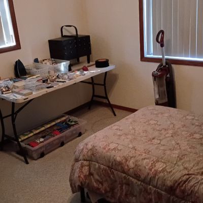 Spare bedroom set up with crafting supplies, a folding utility table, sewing machine cabinet, and a twin bed with a floral comforter.